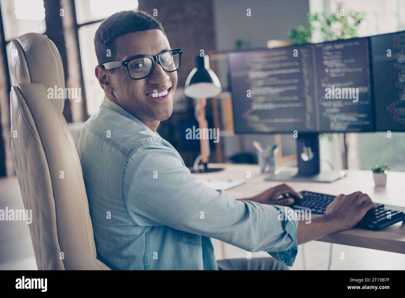 Foto des erfahrenen Programmierers Guy, der die Kamera beim Bearbeiten von Code beim Erstellen einer neuen App am Arbeitsplatz neben dem Computer lächelt Stockfoto