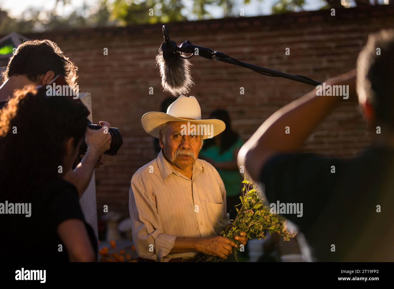 Eine Kamerateam überfordert einen älteren Mann, der während des Festivals Día de Muertos auf dem alten Friedhof am 31. Oktober 2013 in Xoxocotlan, Oaxaca, Mexiko, Blumen auf das Grab seiner Frau legt. Stockfoto