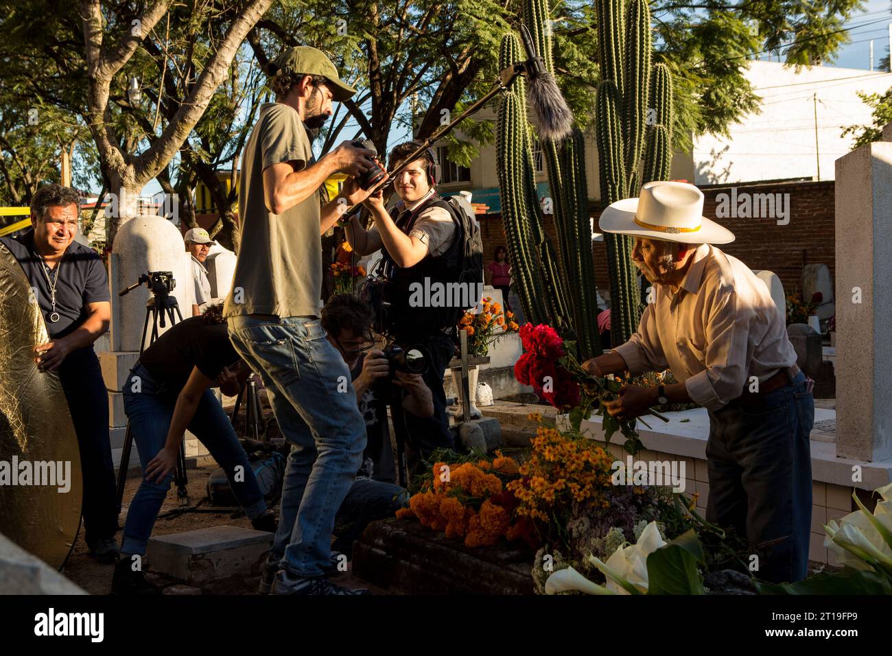 Eine Kamerateam überfordert einen älteren Mann, der während des Festivals Día de Muertos auf dem alten Friedhof am 31. Oktober 2013 in Xoxocotlan, Oaxaca, Mexiko, Blumen auf das Grab seiner Frau legt. Stockfoto