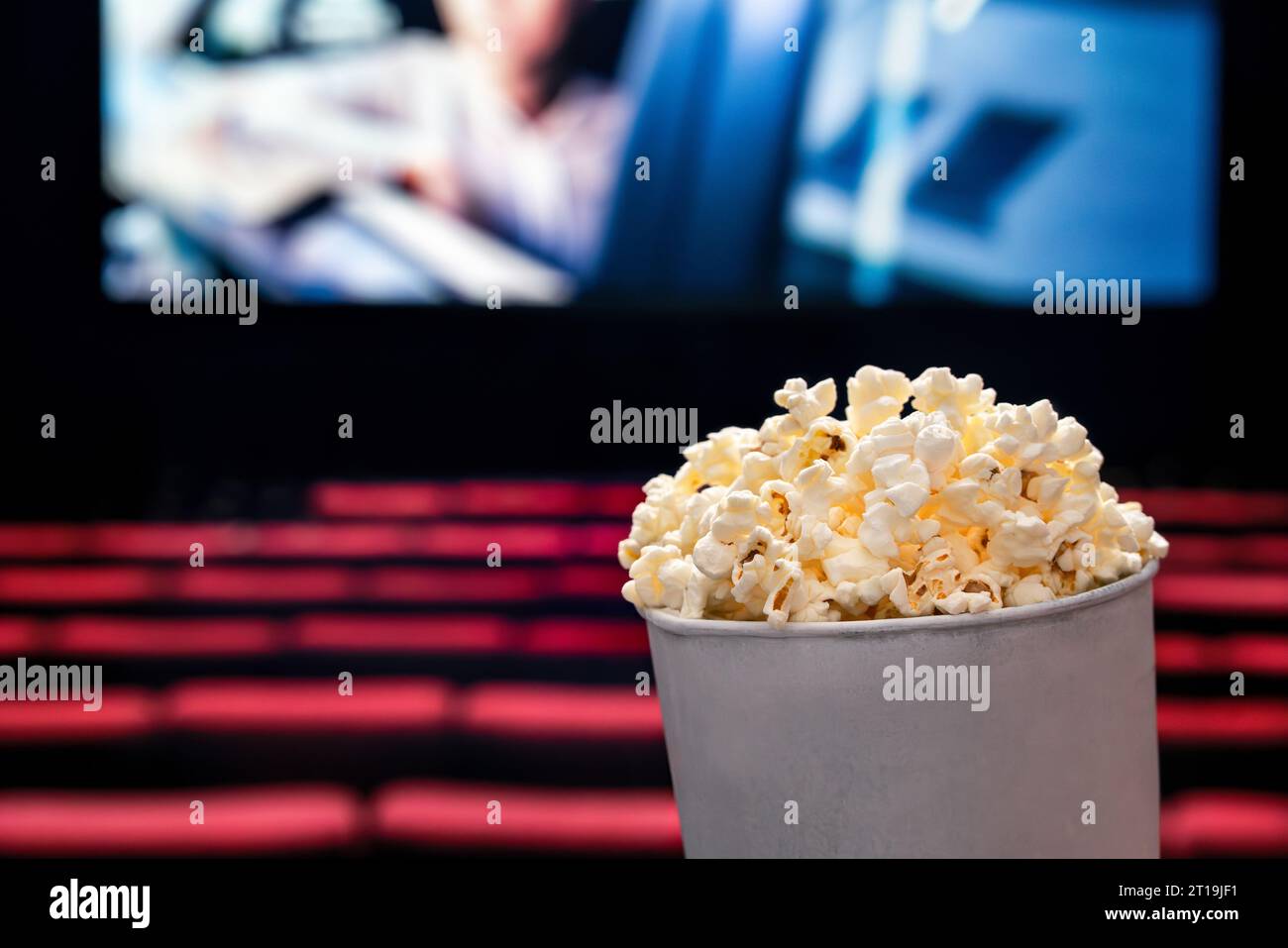 Filme und Popcorn. Popcorn im Kino. Familienfilmnächtekonzept. Action oder romantische Comedy-Unterhaltung auf dem Bildschirm. Dunkles Theater mit roten Sitzen. Stockfoto