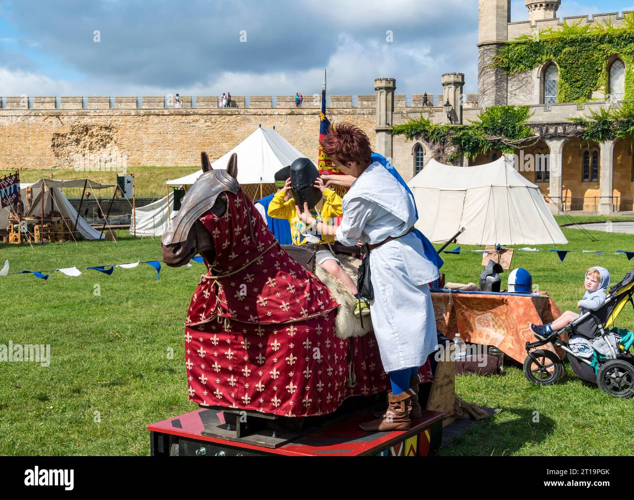 Helferin, die einen Helm auf einen kleinen Jungen setzt, der auf einem Reitpferd sitzt, Lincoln Castle, Lincoln City, Lincolnshire, England, UK Stockfoto