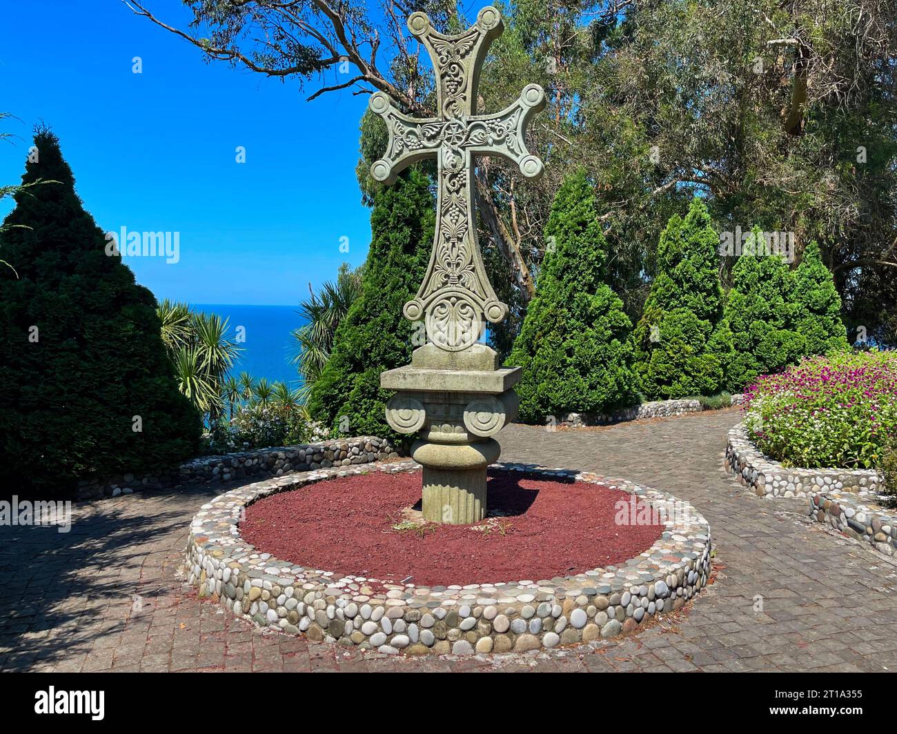 Ein antikes Steinkreuz im Vordergrund eines üppigen Gartens im Batumi Botanical Garden Stockfoto