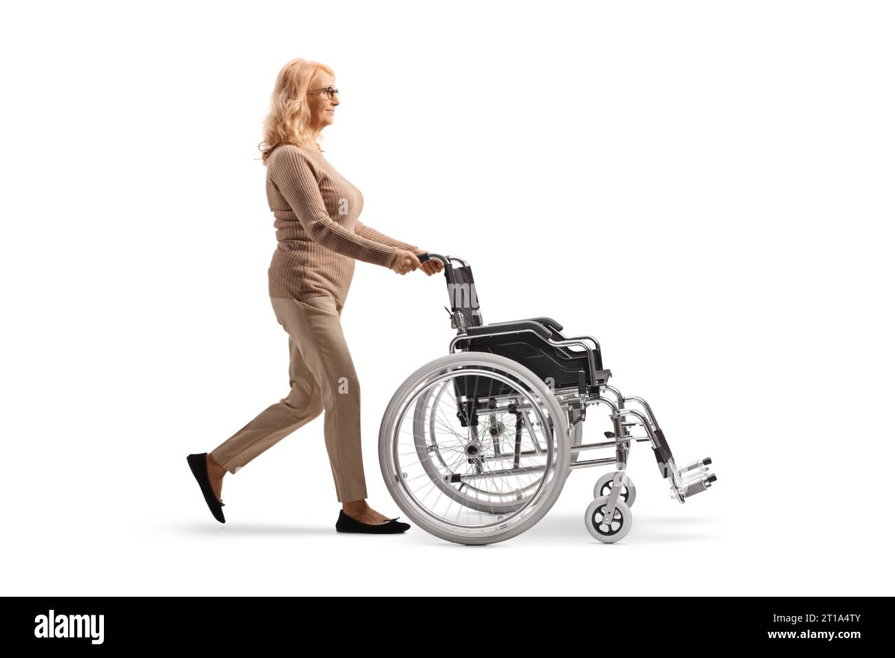 Profilaufnahme einer Reifen Frau, die einen leeren Rollstuhl auf weißem Hintergrund läuft und schiebt Stockfoto
