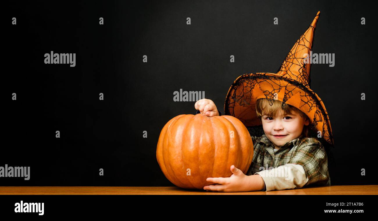 Frohes Halloween. Lächelnder Junge im Hexenhut mit Halloween-Kürbis. Ein kleiner Zauberer mit Jack-o-Laterne, der sich auf die Halloween-Feiertage vorbereitet Stockfoto