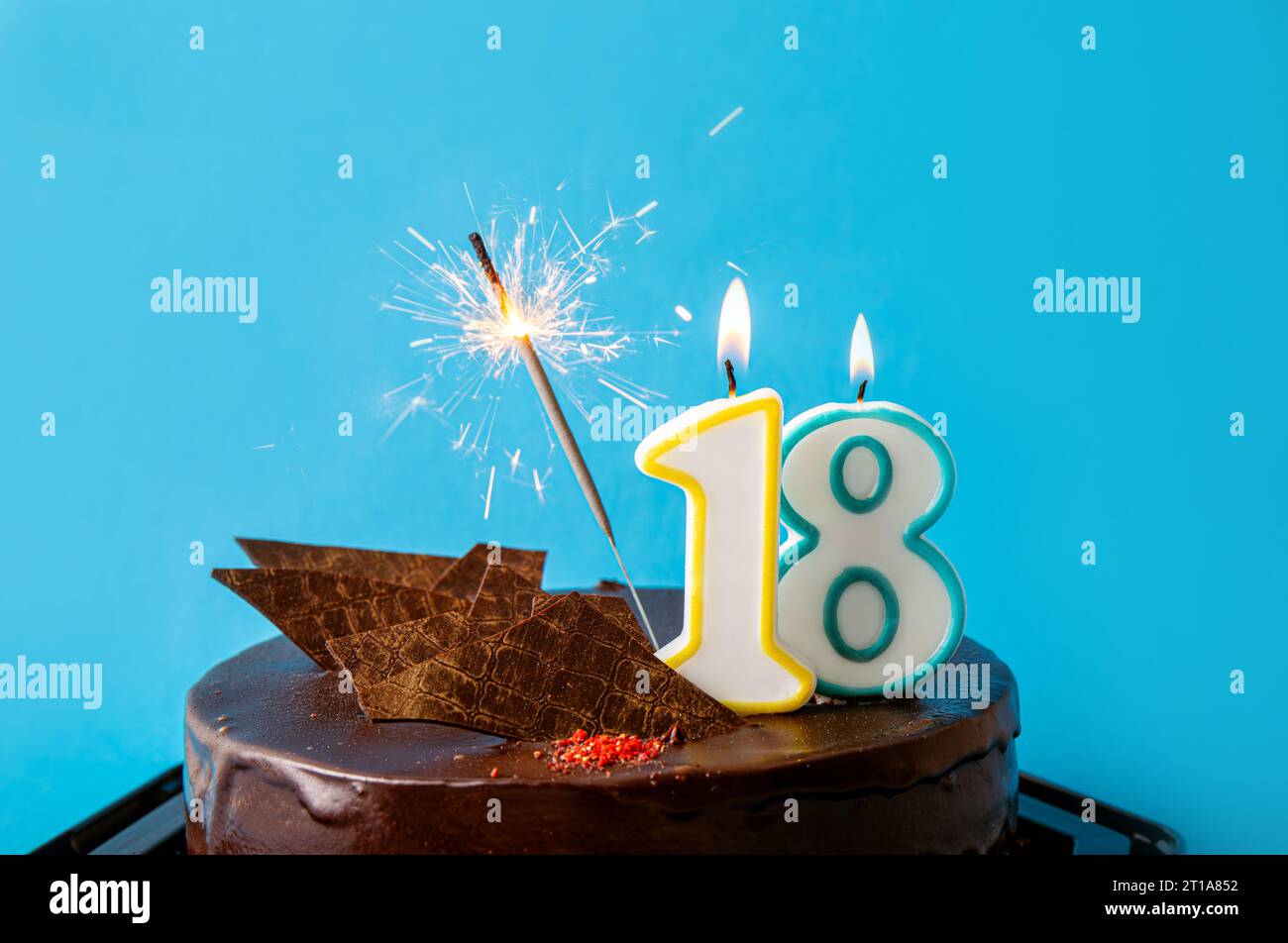 Geburtstagskerze Nr. 18 brennt auf Kuchen, Funken fliegen. Das Konzept zur Feier des achtzehnten Geburtstags oder Jubiläums. Viel Kopierraum auf Blau Stockfoto
