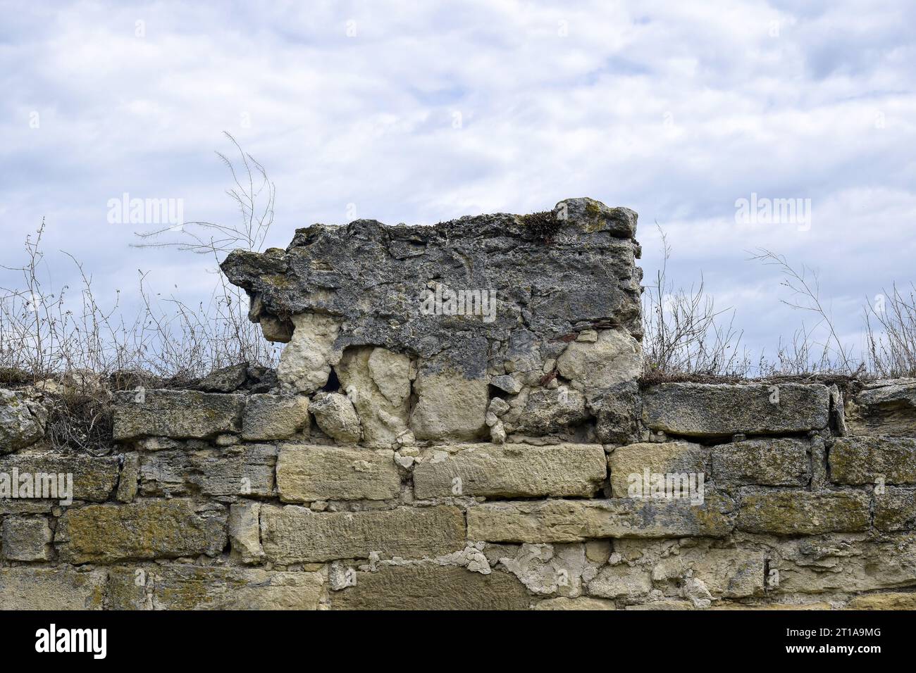 Eine alte Mauer eines alten Steingebäudes, zerstört durch die Zeit mit trockenem Gras auf dem Hintergrund eines bewölkten Himmels. Kopierbereich. Selektiver Fokus. Stockfoto Eine alte Mauer eines alten Steingebäudes, zerstört durch die Zeit mit trockenem Gras auf dem Hintergrund eines bewölkten Himmels. Kopierbereich. Selektiver Fokus. Stockfoto
