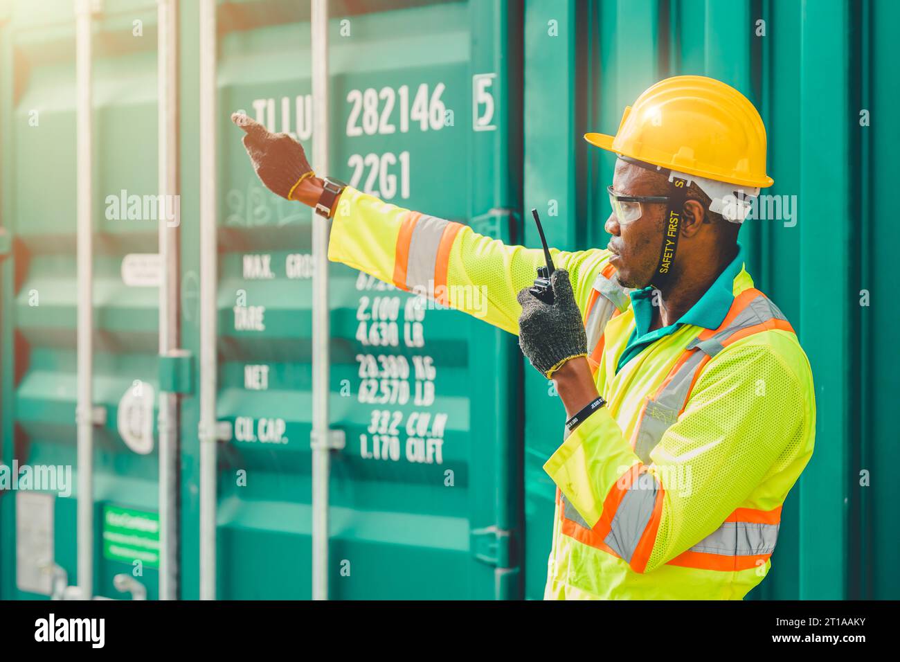 WorkerControl Loading Containers Cargo auf der Hafenwerft mit grünem Farbcontainer für das Image-Konzept der Öko-Logistik-Industrie Stockfoto