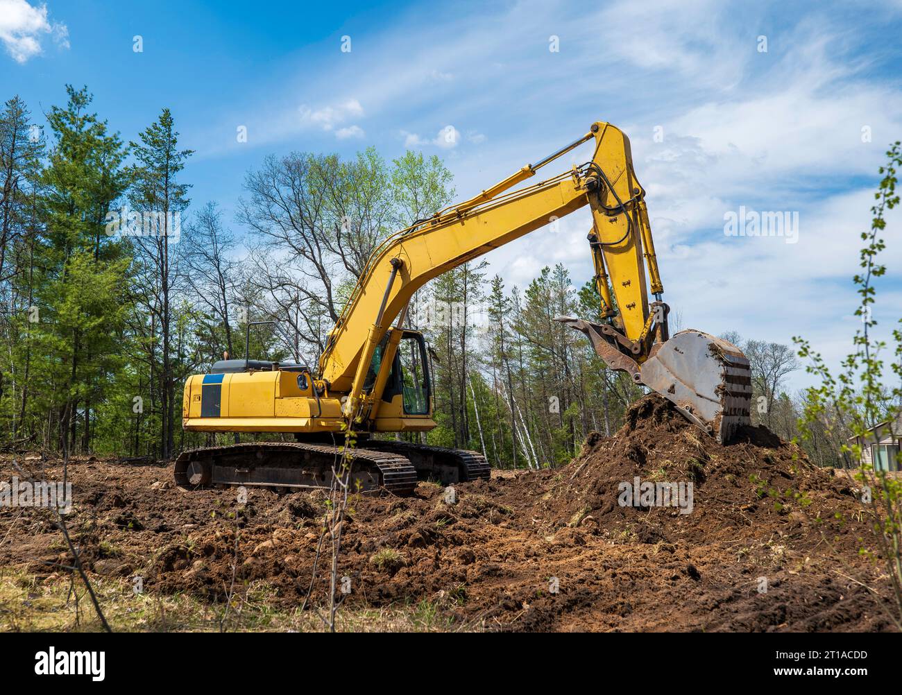 Ein gelber Bagger auf einer zukünftigen neuen Baustelle, dessen Eimer auf einem Schmutzhaufen aufliegt. Stockfoto