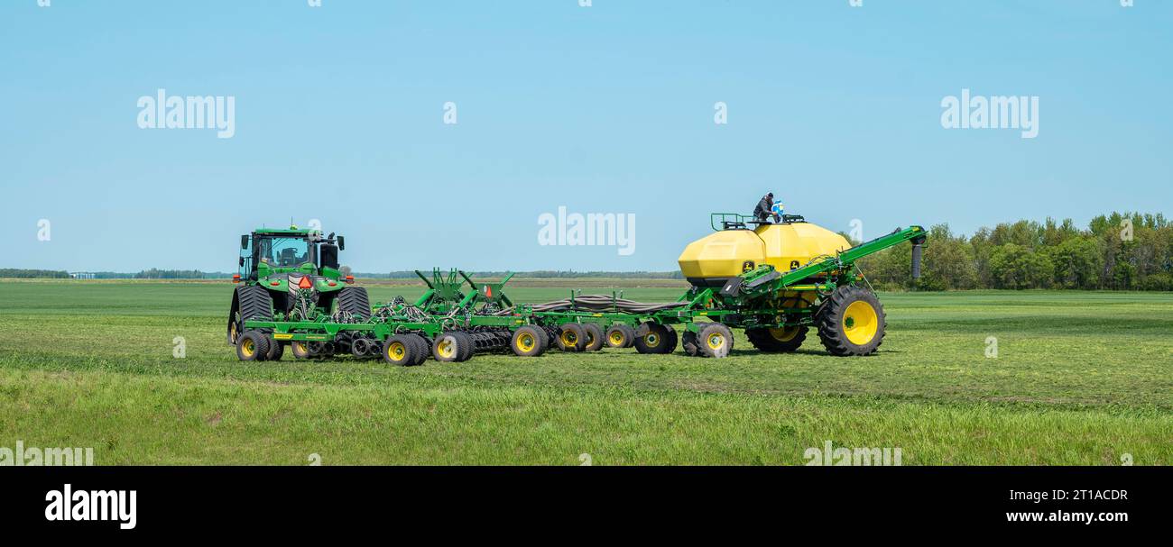 ROSEAU CO, MN – 25. MAI 2023: Ein Landwirt wird auf einem gelben Tank auf einem Anhänger gesehen, der entlang einer Luftbohrmaschine an einem John Deere-Traktor befestigt ist. Stockfoto