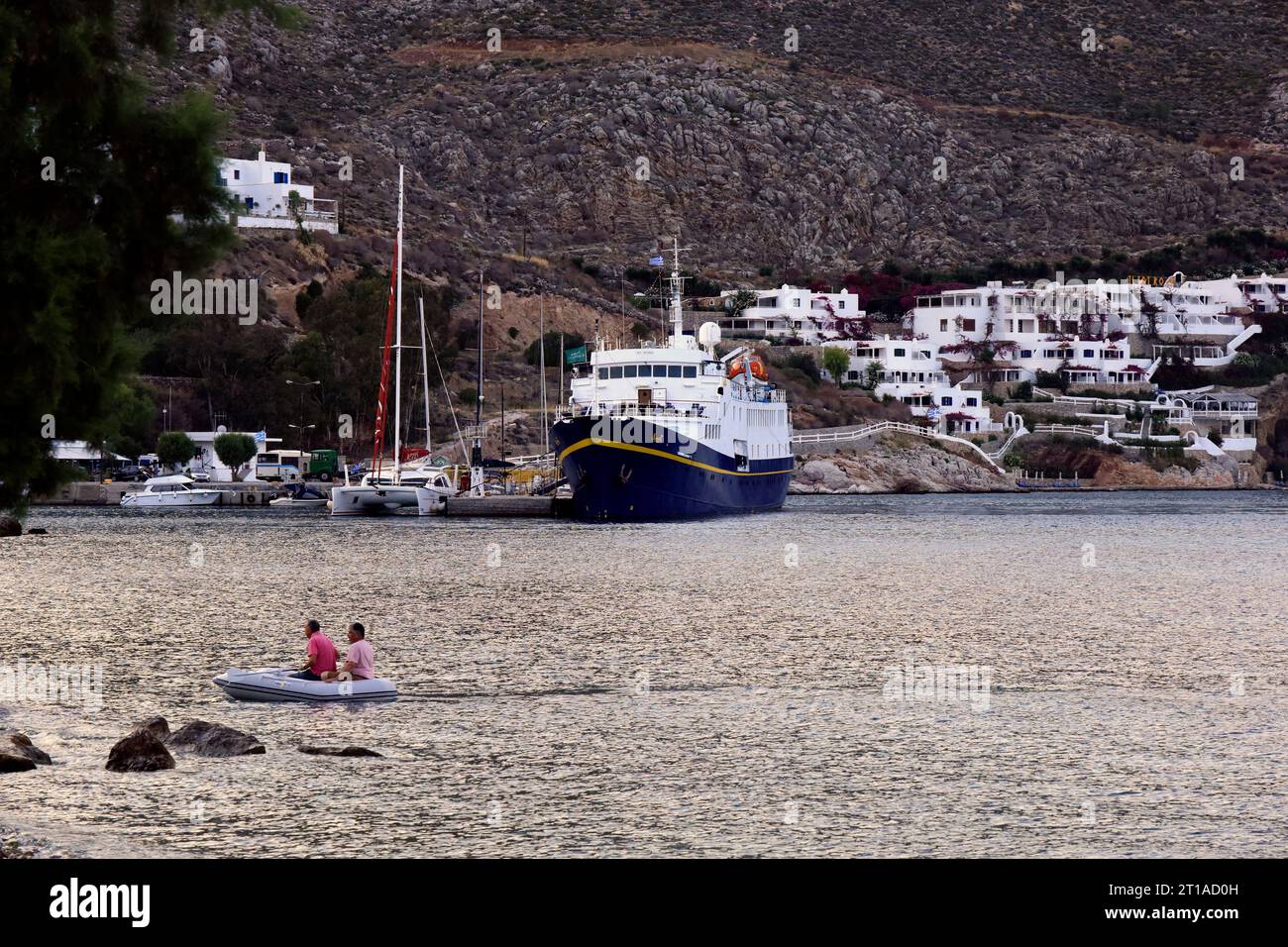 Das Monet-Schiff im Hafen von Livadia und zwei Männer in einem Kautschukschmuck nähern sich der Küste, Livadia Tilos Insel. Vom Juni/Juli 2023. Stockfoto