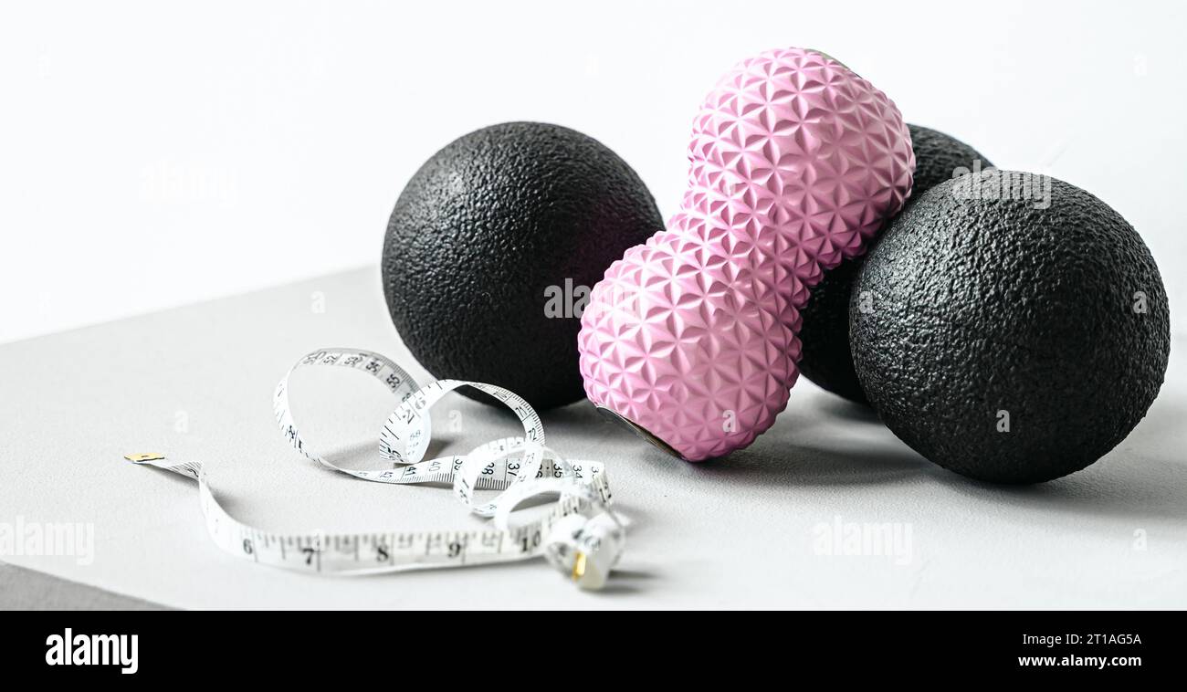 Rosafarbene Erdnusswalze aus Gummischaum, schwarzer Massageball. Yoga, Fitnessgeräte. Zentimeterband zur Messung des Taillenvolumens. Stretching, Pilates Accessori Stockfoto