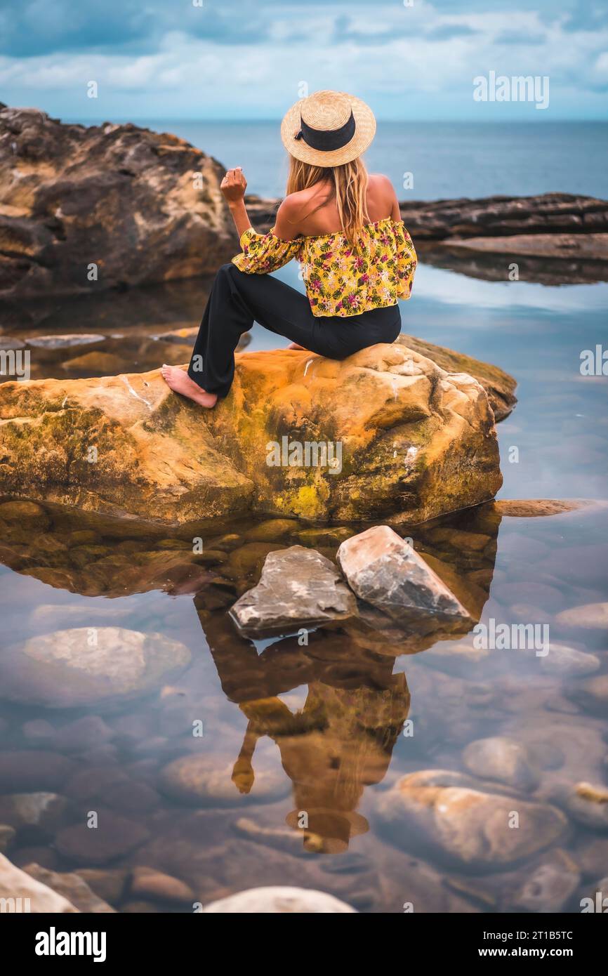 Mädchen in einem Blumenhemd, schwarzen Shorts und Strohhut in einer natürlichen Landschaft am Meer Stockfoto