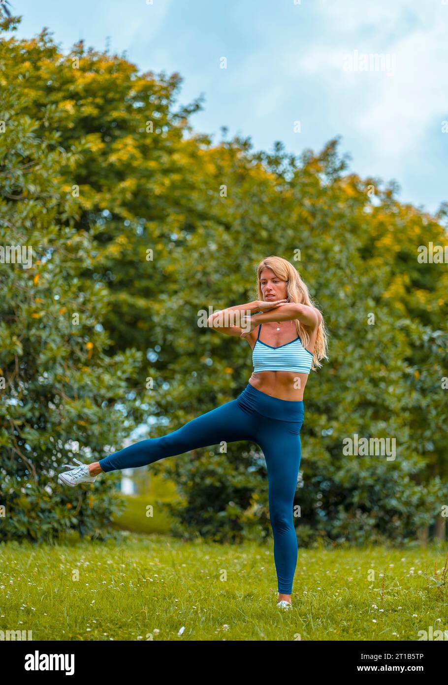 Fitness-Session mit einer jungen blonden Weißen, die auf der Straße trainiert, mit einer blauen maya an den Füßen und einem weißen kurzen Hemd Stockfoto