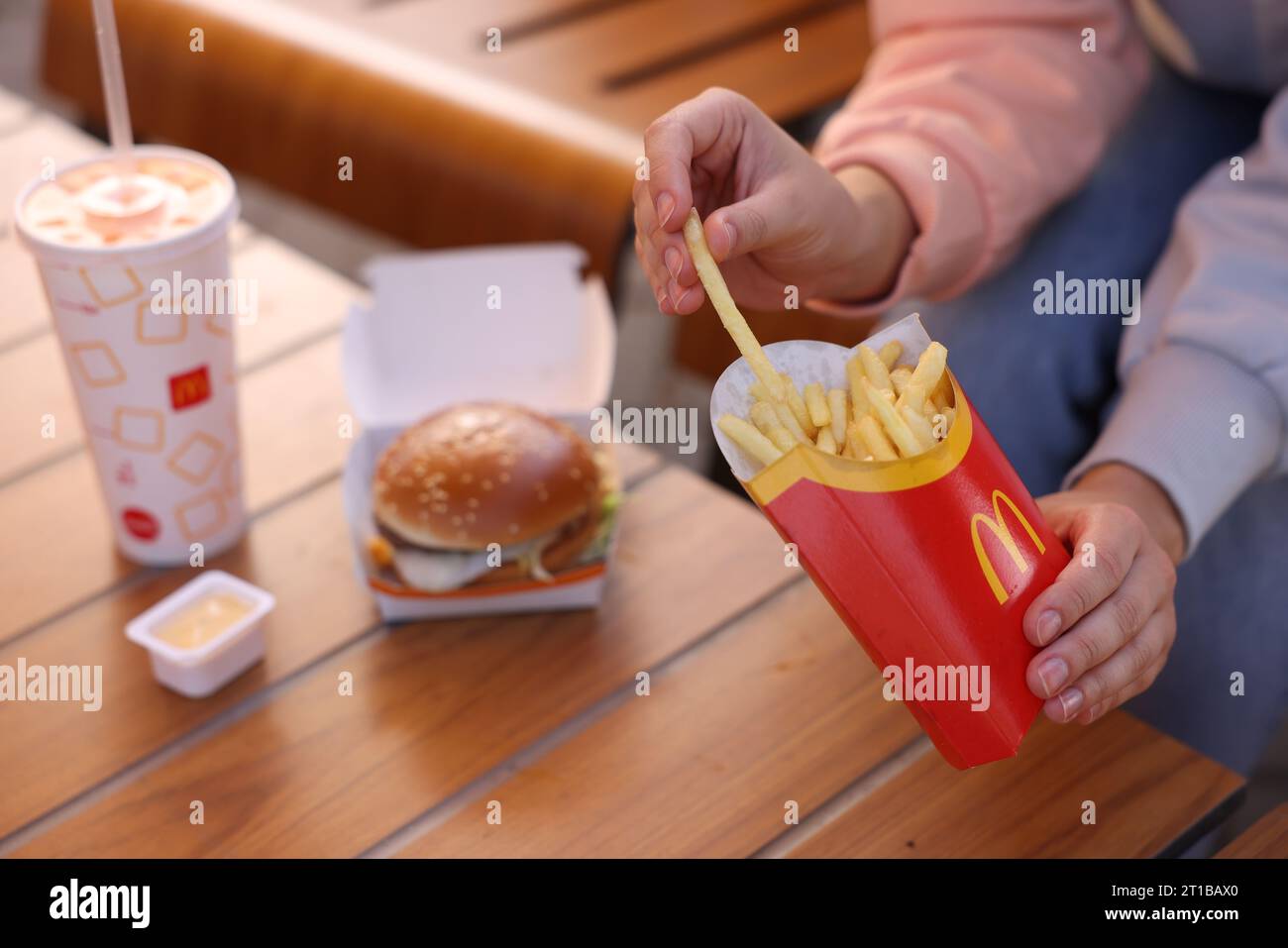 Lviv, Ukraine - 26. September 2023: Frau isst McDonalds Menü am Holztisch im Freien, Nahaufnahme Stockfoto