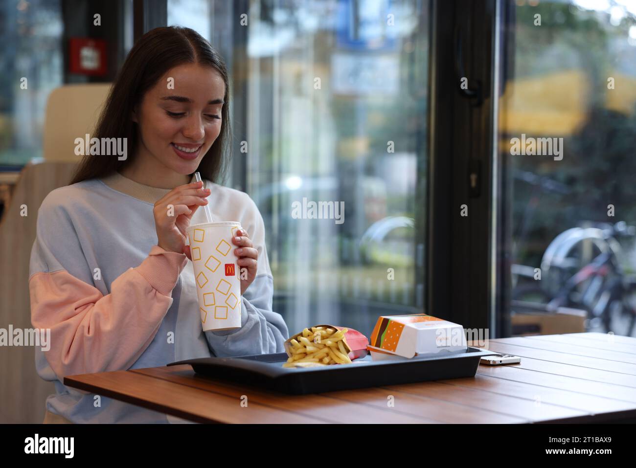 Lviv, Ukraine - 26. September 2023: Frau mit McDonald's Getränk, Burger und Pommes frites am Tisch im Restaurant, Platz für Text Stockfoto