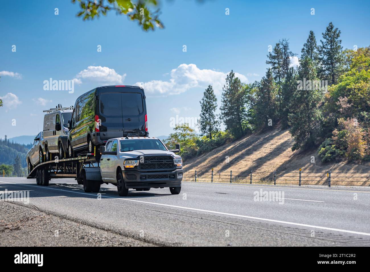 Grauer Industrietransportwagen mit Schwerlastwagen, der Minivans auf dem langen Auflieger auf der Einbahnstraße i transportiert Stockfoto