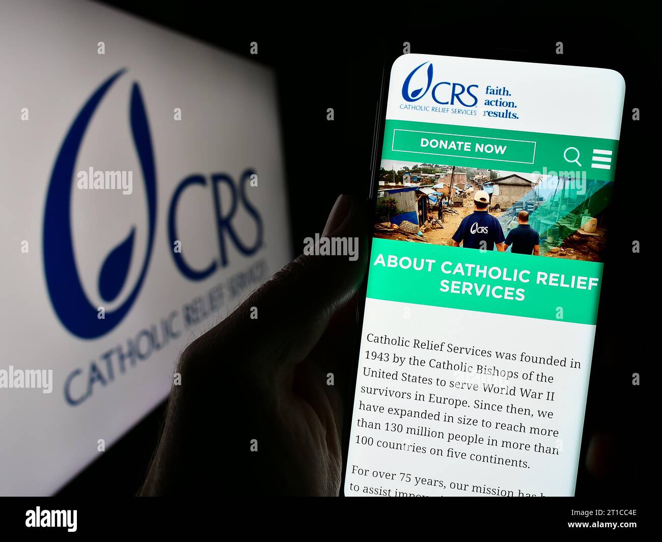 Person mit Smartphone und Website der katholischen Hilfsorganisation Katholische Hilfsdienste (CRS) vor dem Logo. Konzentrieren Sie sich auf die Mitte des Telefondisplays. Stockfoto