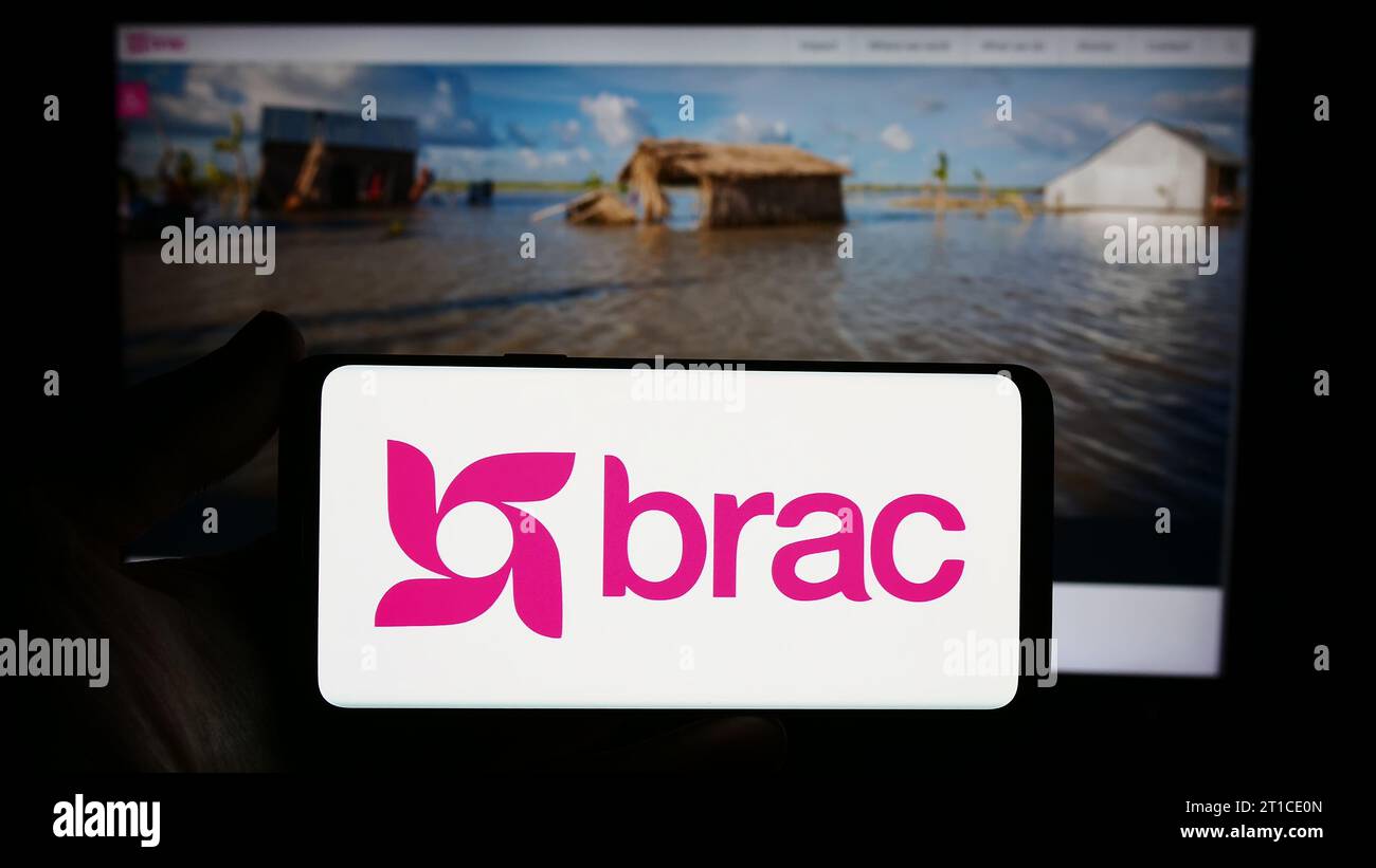 Person mit Smartphone und Logo der internationalen Entwicklungsorganisation BRAC vor der Website. Schwerpunkt auf dem Display des Telefons. Stockfoto