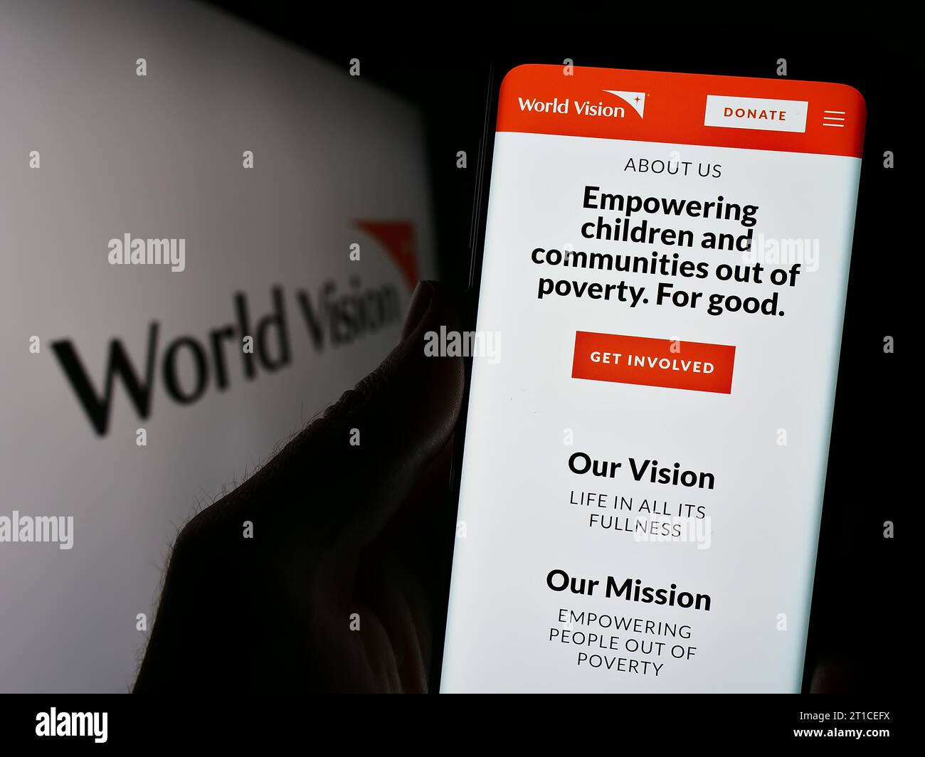 Person mit Smartphone und Webseite der Wohltätigkeitsorganisation World Vision International vor dem Logo. Konzentrieren Sie sich auf die Mitte des Telefondisplays. Stockfoto