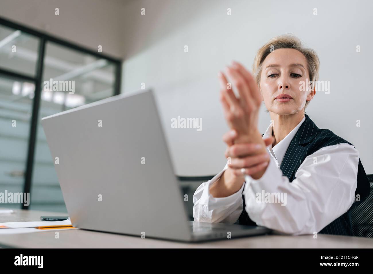 Nahaufnahme einer erschöpften Geschäftsfrau mittleren Alters, die beim Tippen auf einem Laptop am Arbeitsplatz starke Schmerzen im Handgelenk spürt. Stockfoto