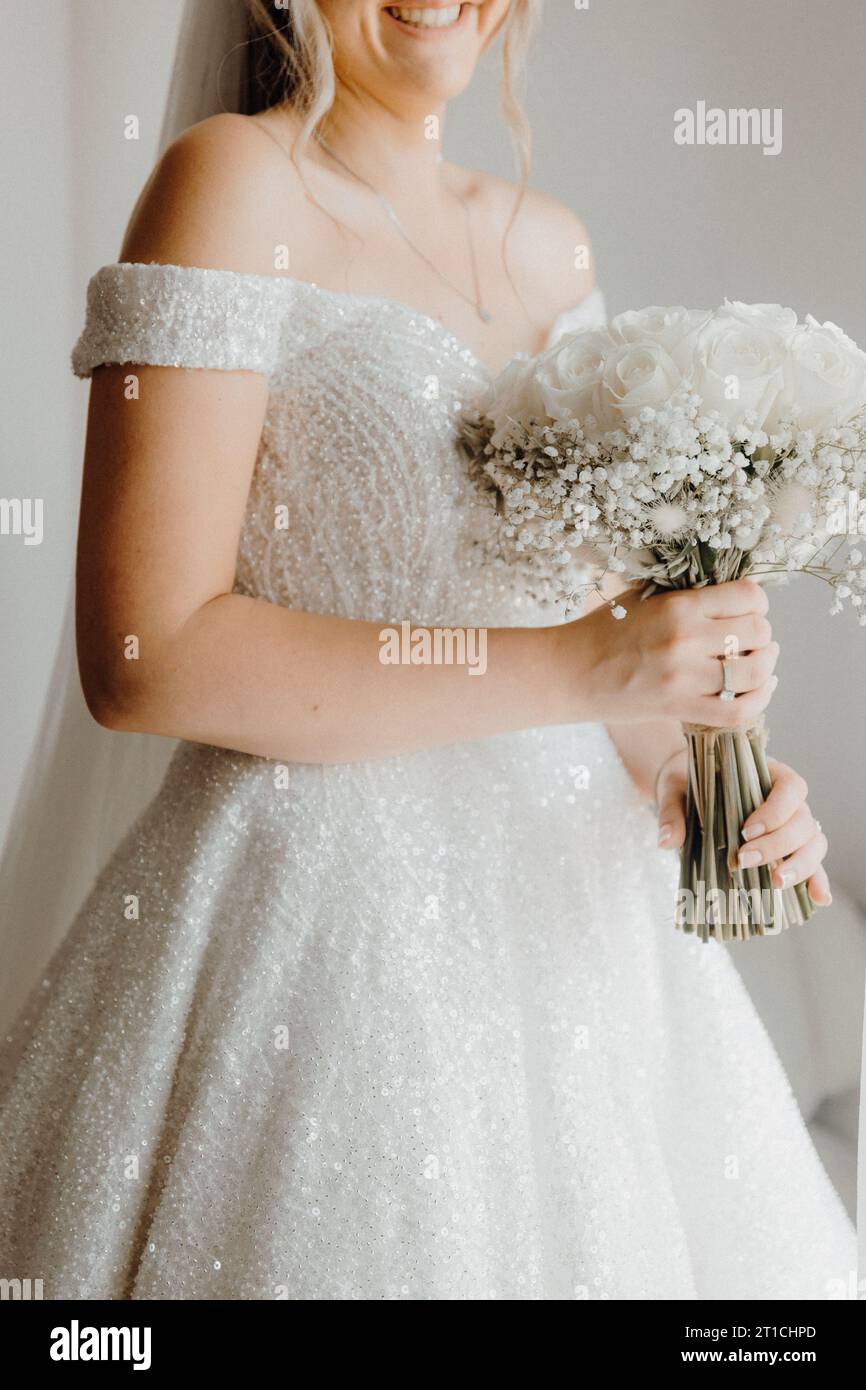 Eine schöne junge Frau, die ein weißes Hochzeitskleid trägt und einen Blumenstrauß aus rosa und weißen Blumen in den Händen hält. Sie steht auf einer Wiese aus hohem Gras Stockfoto