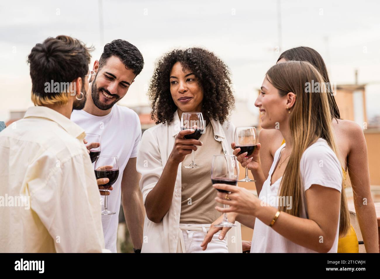 Multirassische Gruppe von Freunden bei Drinks auf einer Dachparty. Vielfältige junge, glückliche Gruppe von Millennials, die Spaß auf einer Terrasse haben. Stockfoto