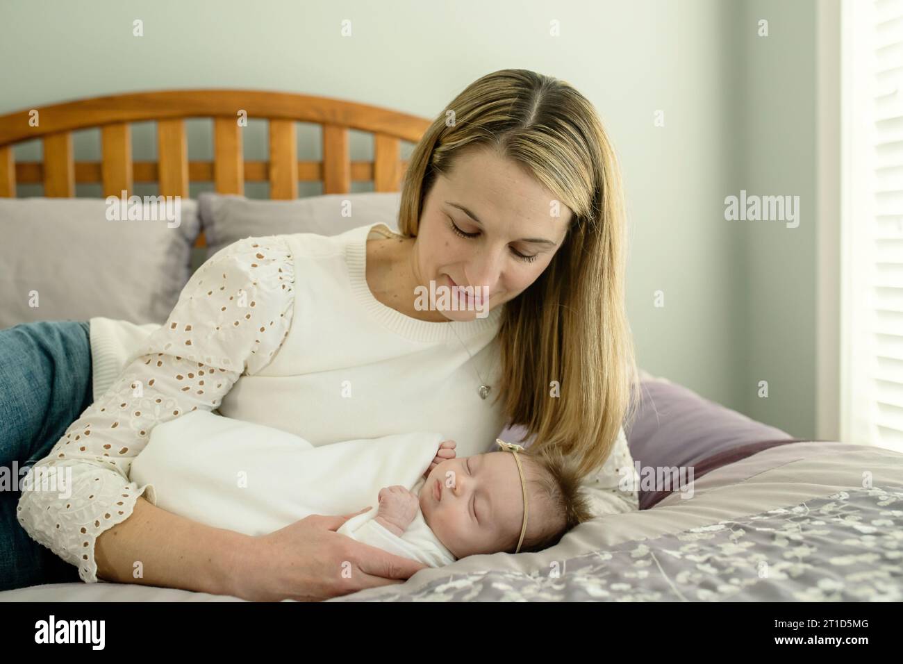 Mutter und Neugeborenes liegen auf dem Bett; Mutter blickt hinunter auf das lächelnde Baby Stockfoto