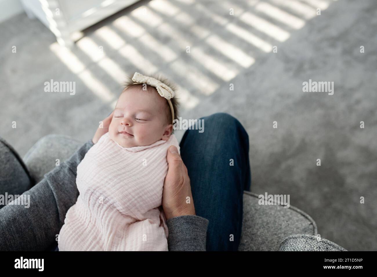 Verschlafenes Neugeborenes lächelt, in Papas Arme gewickelt Stockfoto