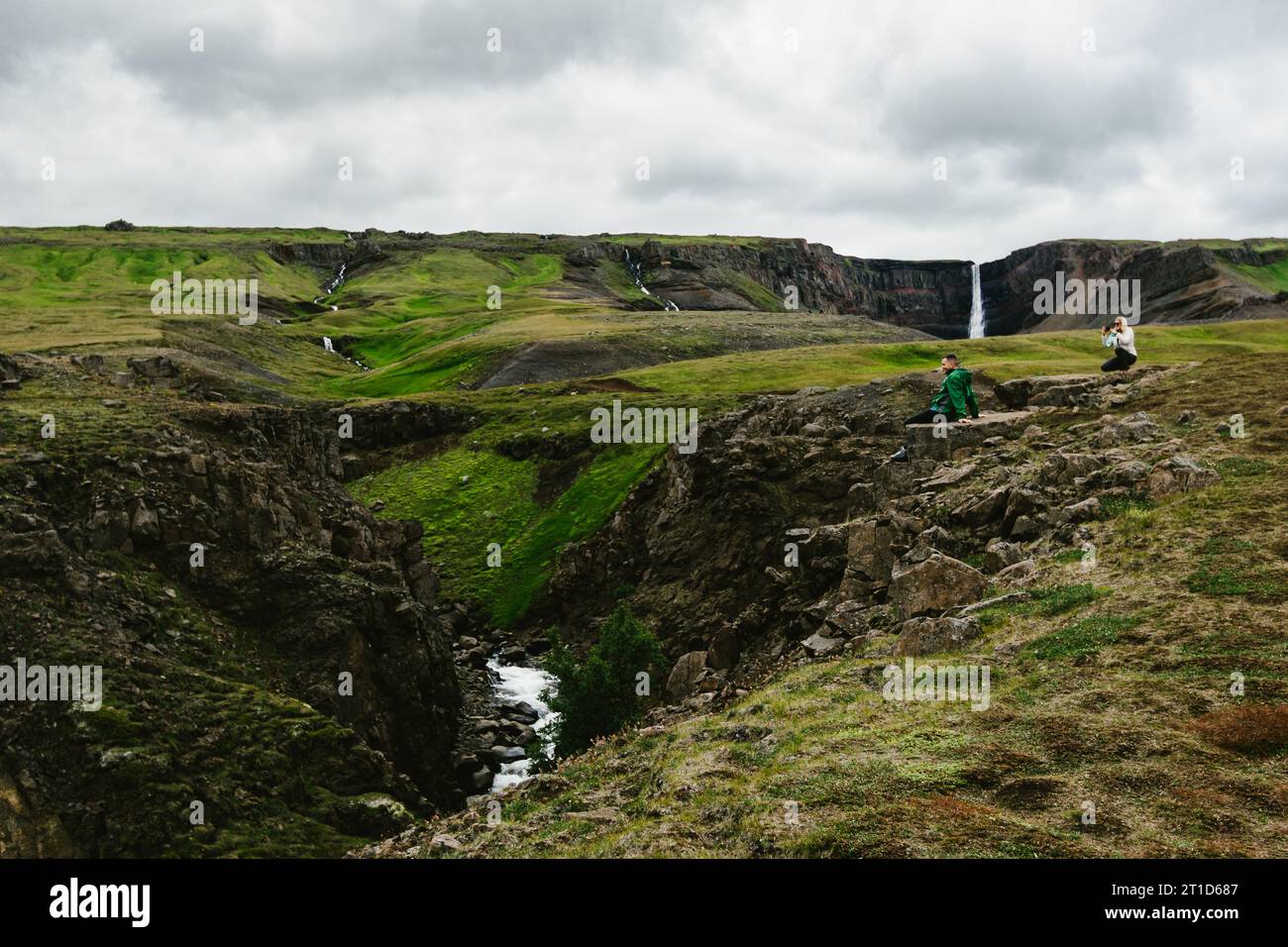 Frau fotografiert Mann mit Telefon an grünen Hügeln und Wasserfall Stockfoto