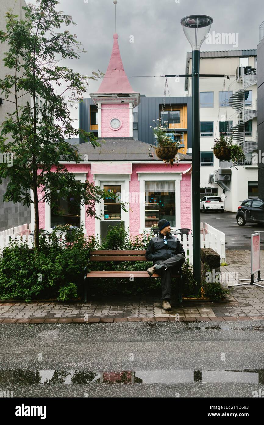 Mann auf der Bank vor der hübschen pinken Straßenszene Stockfoto