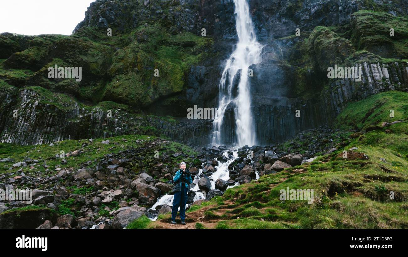 Frau auf grünen Berghügeln mit Wasserfall und Klippen Stockfoto