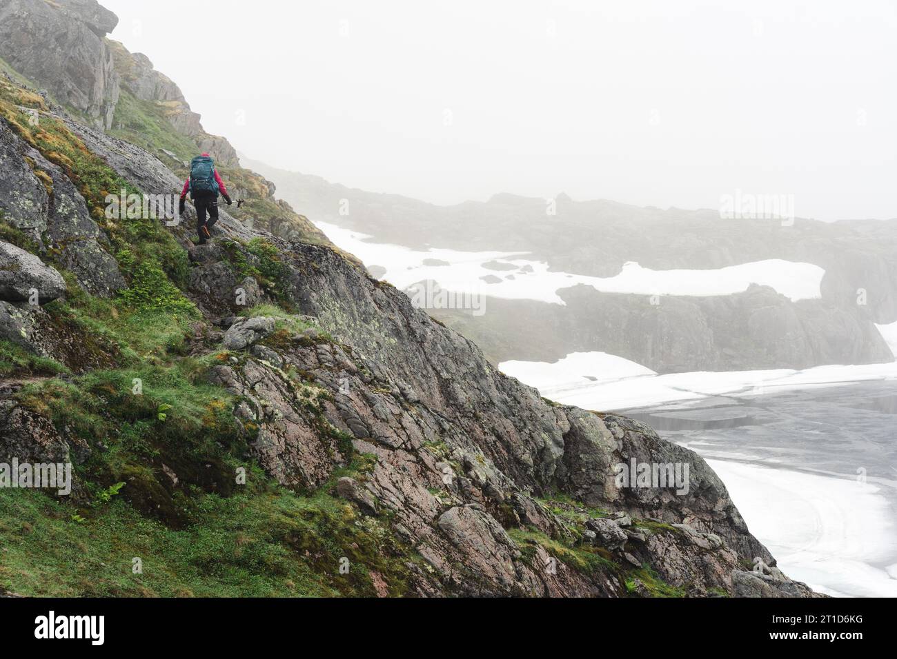 Eine Frau, die die felsige Küste des gefrorenen Bergsees hinaufwandert Stockfoto