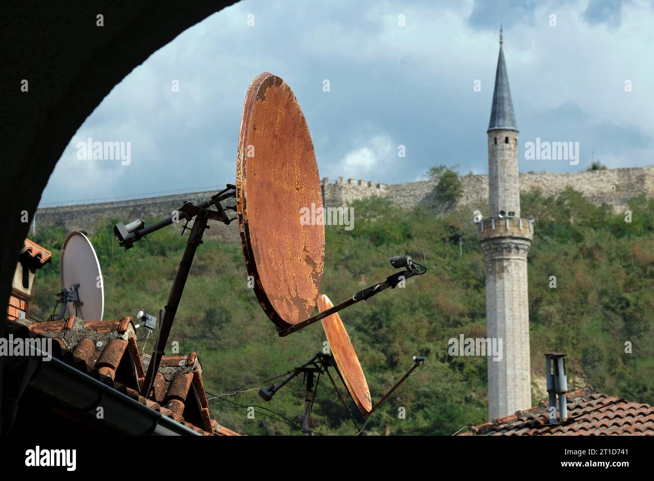 Rostige Satellitenschüsseln auf Dächern in Prizren, Kosovo, mit einem Minarettturm im Hintergrund Stockfoto