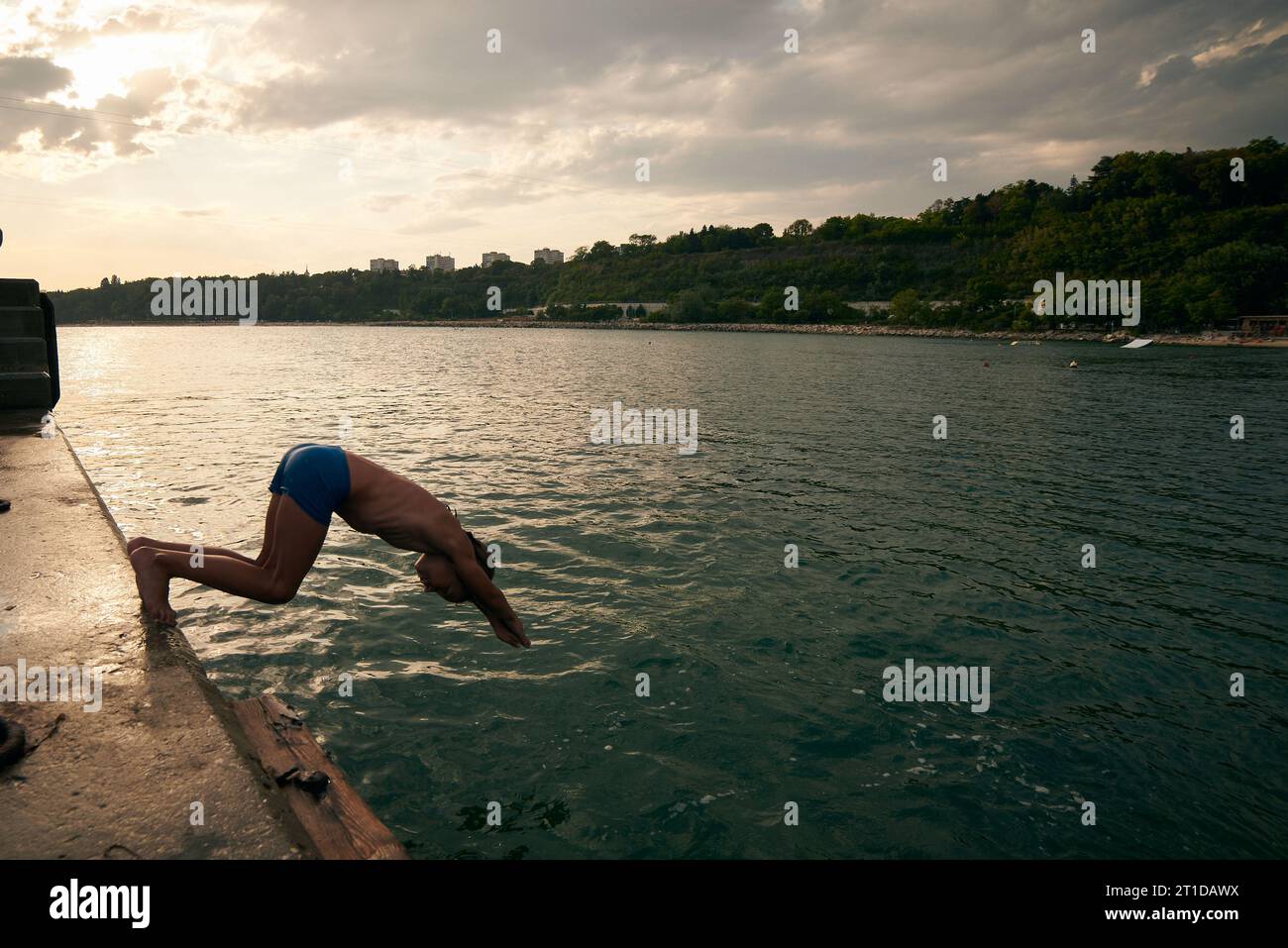 Der 8-jährige Junge taucht von einem Pier ins Meer. Heißer Sommertag. Stockfoto