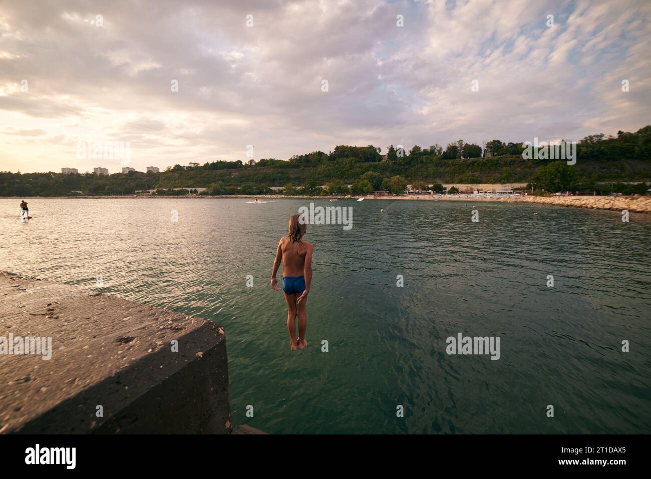 Der 8-jährige Junge taucht von einem Pier ins Meer. Heißer Sommertag. Stockfoto