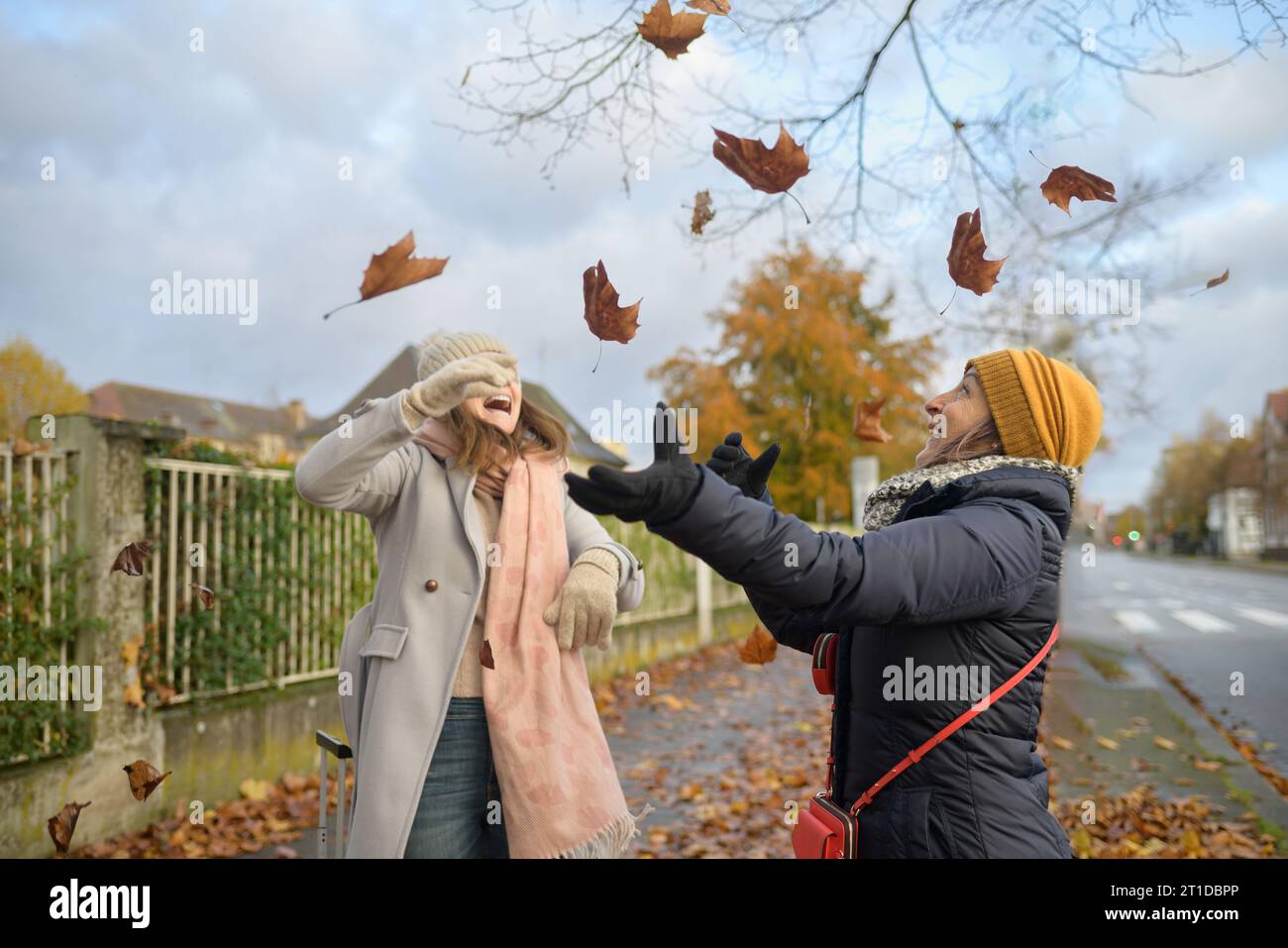 Ein paar glückliche Frauen, die in warmer Kleidung mit den Blättern in der Stadt spielen Stockfoto