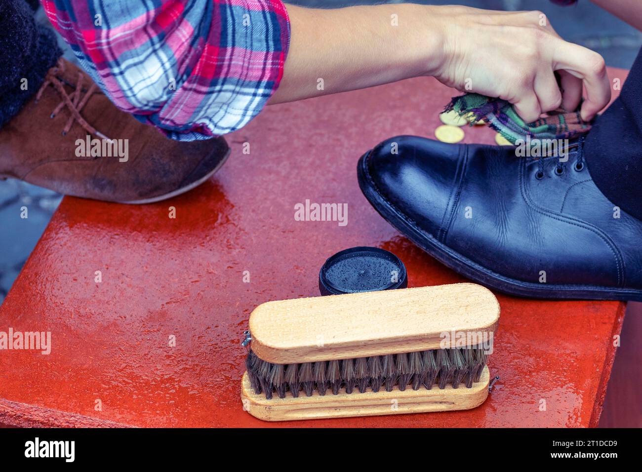 Schuhcreme, Pinsel-Nahaufnahme. Reinigung der Stiefel auf der Straße. Konzept falsche Pflege von Schuhen. Herrenschuh mit rechtem Fuß auf traditionellem Stiefelschaber W Stockfoto