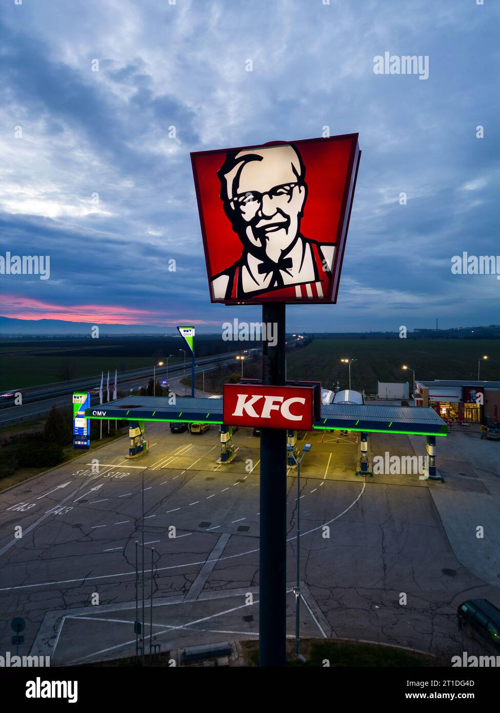 Belozyom, Bulgarien - 24. dezember 2022 Schild für das KFC-Fast-Food-Restaurant an der OMV-Tankstelle auf einer Autobahn bei abendlicher Luftansicht. Stockfoto