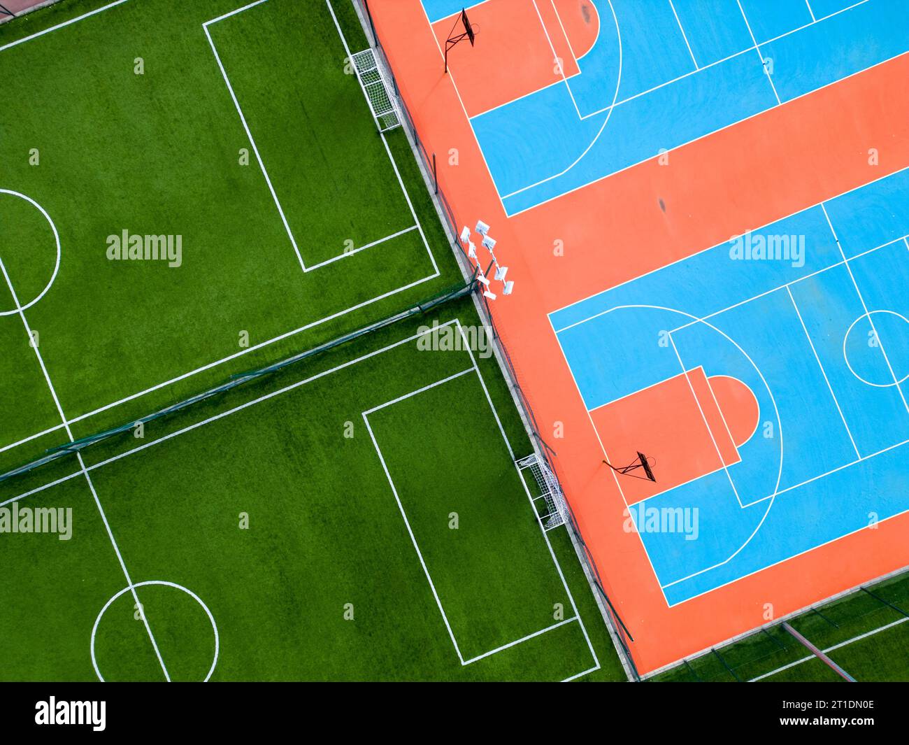 Aus der Vogelperspektive auf ein grünes Fußballfeld und einen farbenfrohen Basketballplatz, der einen Blick auf zwei verschiedene Sporteinrichtungen nebeneinander bietet. Das Gegenteil Stockfoto