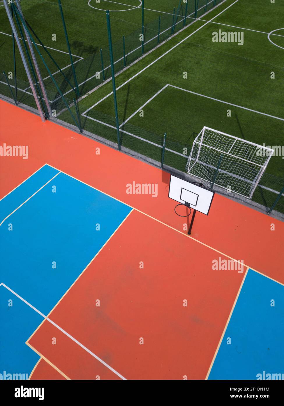 Aus der Vogelperspektive auf ein grünes Fußballfeld und einen farbenfrohen Basketballplatz, der einen Blick auf zwei verschiedene Sporteinrichtungen nebeneinander bietet. Das Gegenteil Stockfoto