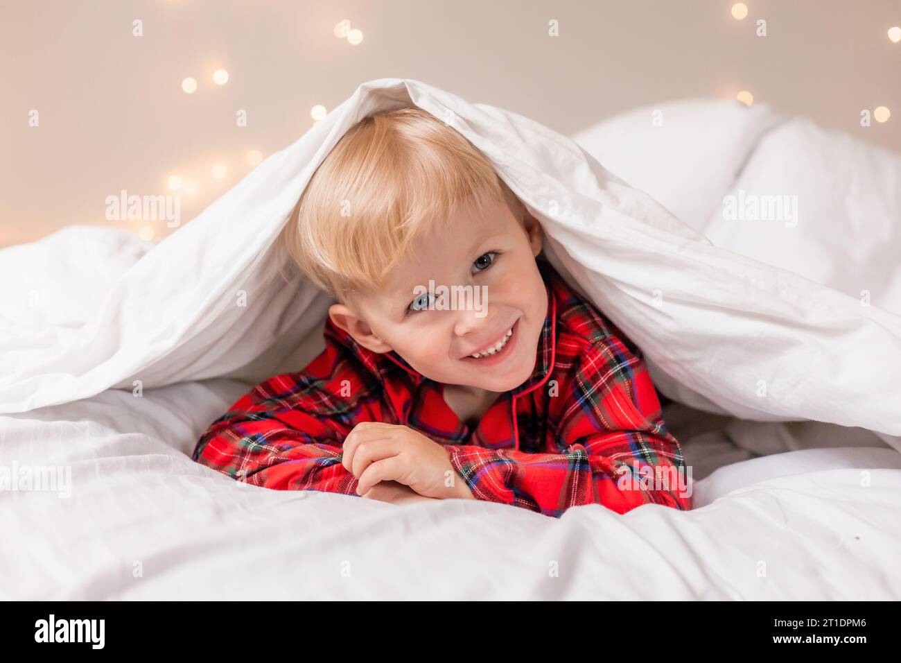 Der lächelnde blonde Junge im roten Pyjama liegt im Bett. Hochwertige Fotos Stockfoto