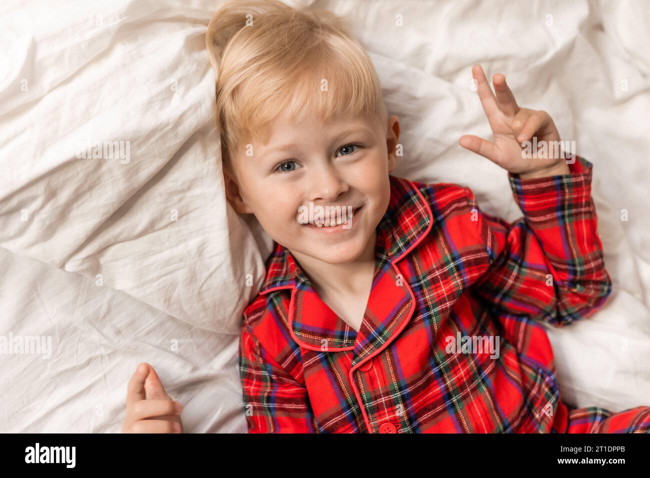 Der lächelnde blonde Junge im roten Pyjama liegt im Bett. Hochwertige Fotos Stockfoto