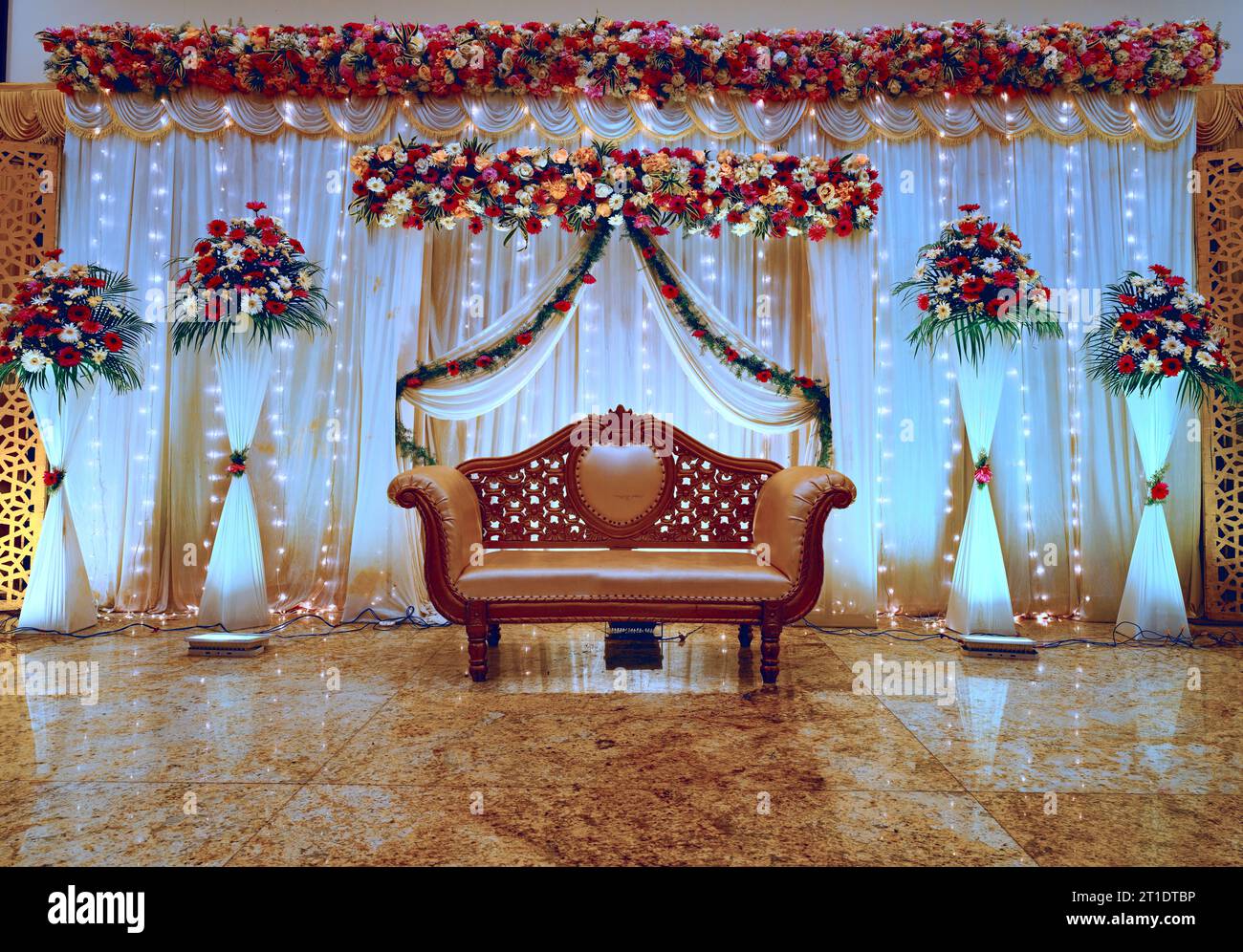 Ein dekoriertes Bühnenbild für einen Hochzeitsempfang mit Vorhängen, Tüchern und Blumen, wunderschön eingerichtet mit einem Sofa in der Mitte, damit das Paar sitzen kann Stockfoto