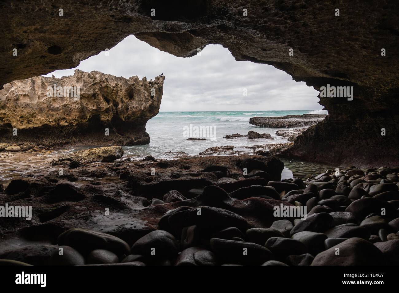 Wenn Sie von der Höhle aus blicken, offenbart sich ein felsiger Felsvorsprung, der vom Meer umgeben ist, während das Innere der Höhle mit einer Reihe von Felsen gefüllt ist Stockfoto