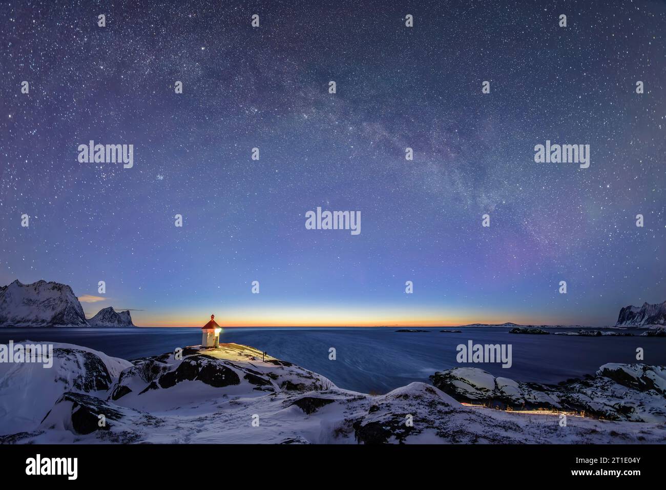 Der beleuchtete Leuchtturm steht auf einer Landzunge mit schneebedeckten Bergen und Sternenhimmel mit Milchstraße, Senja, Troms og Finnmark, Norwegen Stockfoto