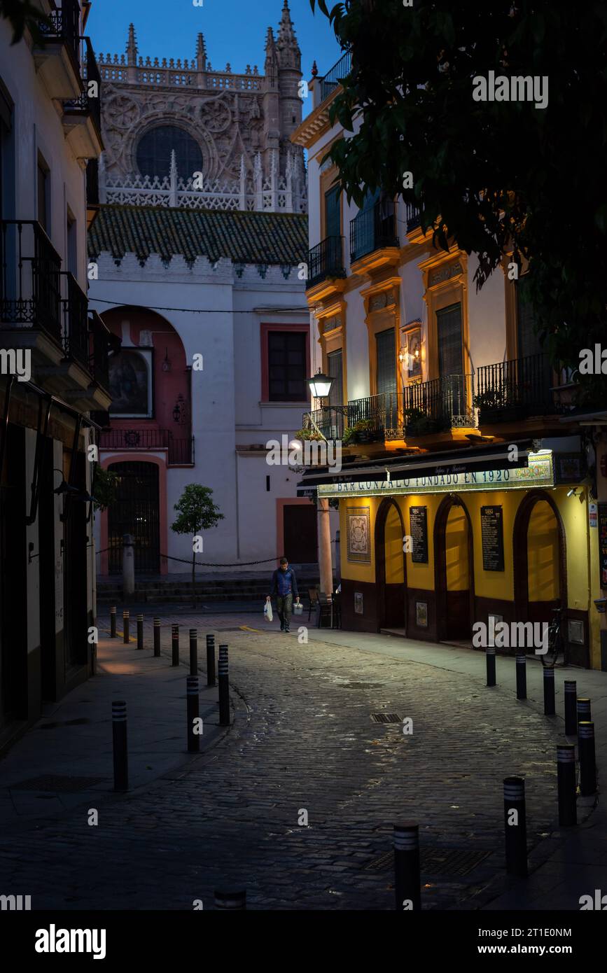 Am frühen Morgen schlendert in Sevilla, Spanien, ein Mann eine Straße hinunter, die von der Lichtquelle beleuchtet wird, im antiken Stadtteil. Stockfoto