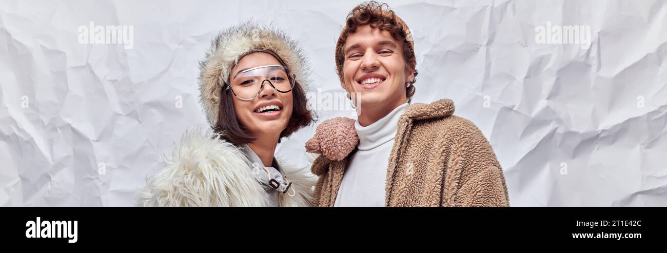 Glückliches interrassisches Paar in stilvoller Winterkleidung, das die Kamera vor weißem Hintergrund betrachtet, Banner Stockfoto