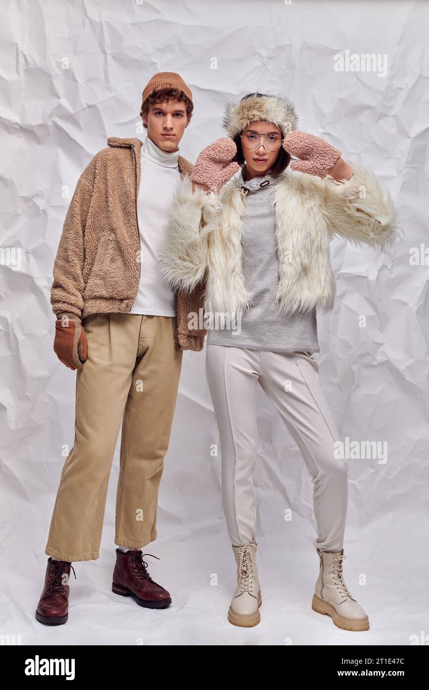 Die ganze Länge eines modisch gekleideten, interrassischen Paares vor weißem Hintergrund, winterlicher Stil Stockfoto