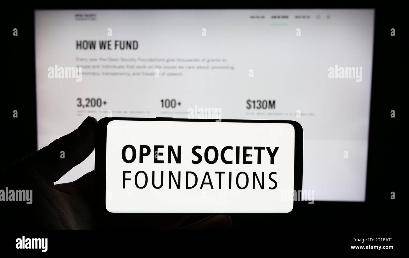 Person mit Smartphone und Logo der Organisation Open Society Foundations (OSF) vor der Website. Schwerpunkt auf dem Display des Telefons. Stockfoto