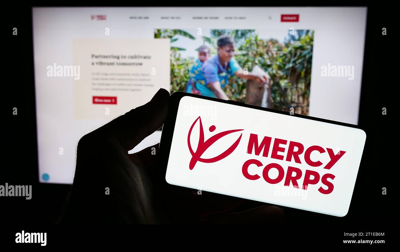 Person mit Smartphone und Logo der US-Hilfsorganisation Mercy Corps vor der Website. Schwerpunkt auf dem Display des Telefons. Stockfoto